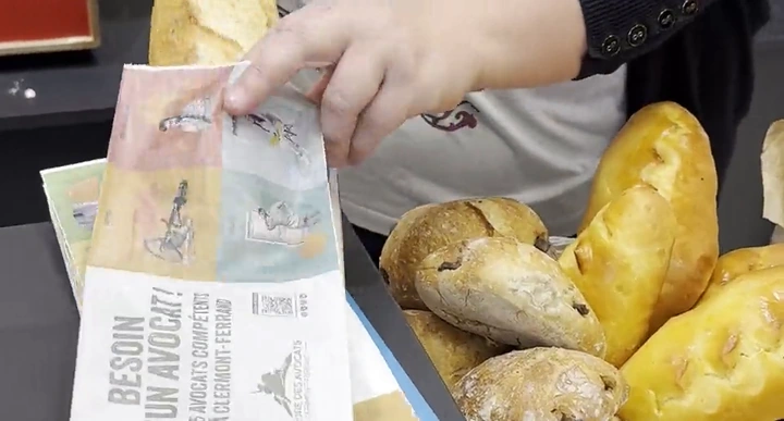 Sac à pain publicitaire d'un cabinet d'avocats, posé sur le comptoir d'une boulangerie à côté des baguettes